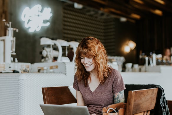 a woman smiling at her laptop in a cafe.